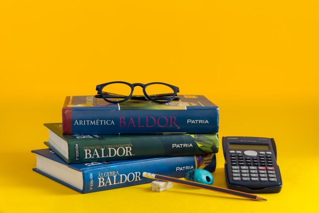 Uma Pilha De Livros E Uma Calculadora Em Um Fundo Amarelo 7ub1eAqc2vw