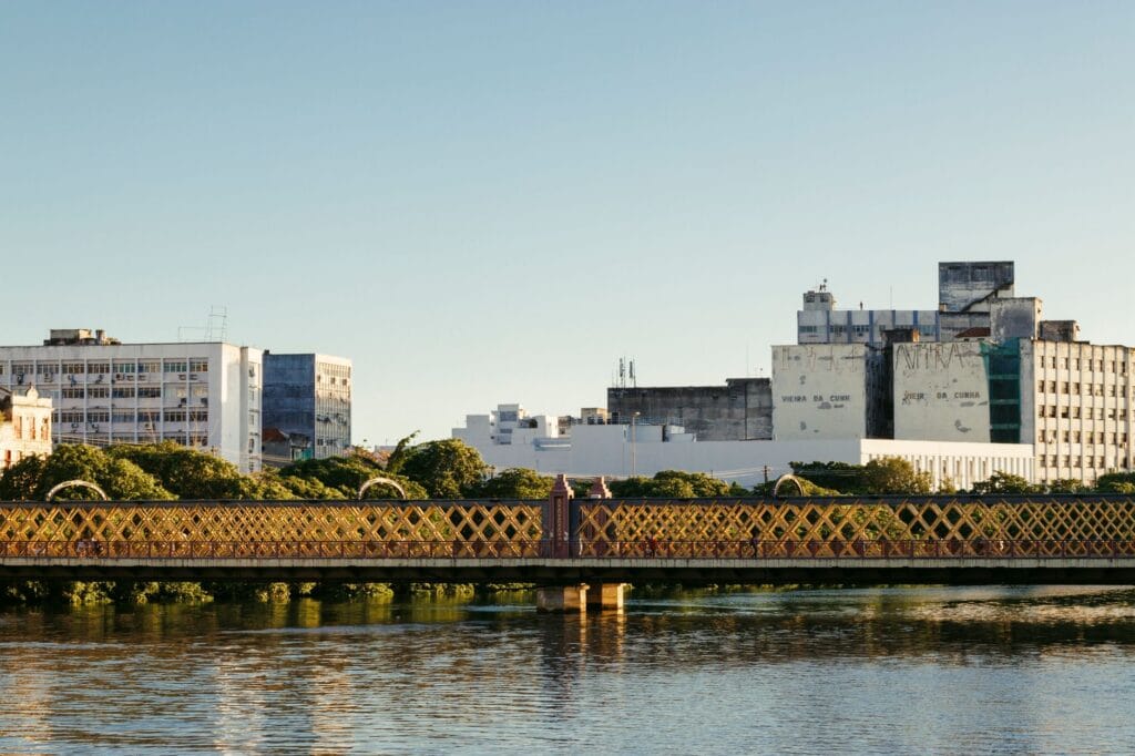 Serene view of a heritage bridge and urban skyline reflecting in calm waters during the day.