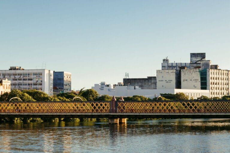Serene view of a heritage bridge and urban skyline reflecting in calm waters during the day.
