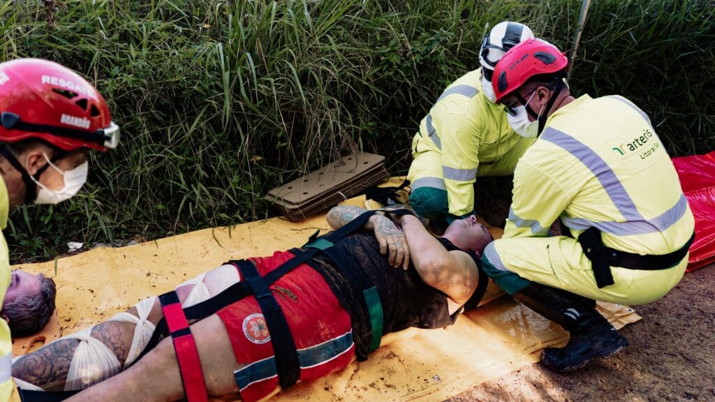 Rescue operation with paramedics attending to an injured person outdoors. Wearing protective helmets and face masks.