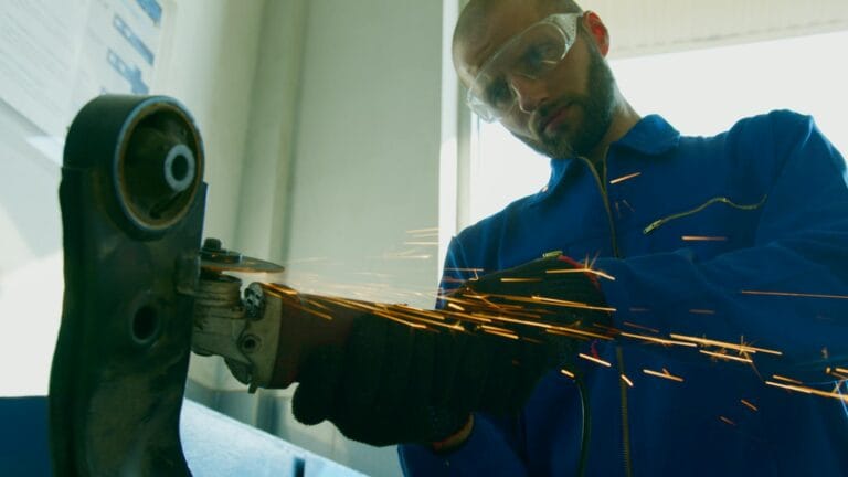 A mechanic wearing protective gear operates a grinder, creating sparks in a workshop setting.