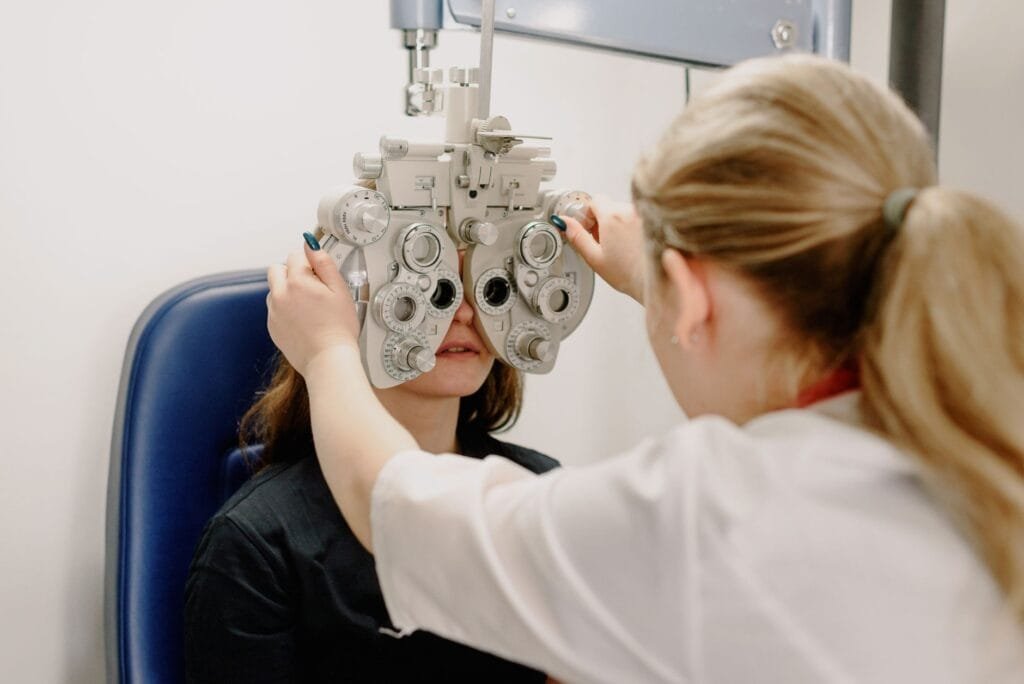 Anonymous female doctor in medical uniform doing eyesight measurement of patient with modern phoropter with lenses in contemporary clinic