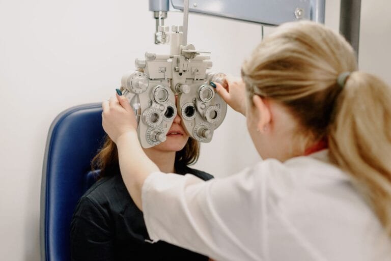 Anonymous female doctor in medical uniform doing eyesight measurement of patient with modern phoropter with lenses in contemporary clinic