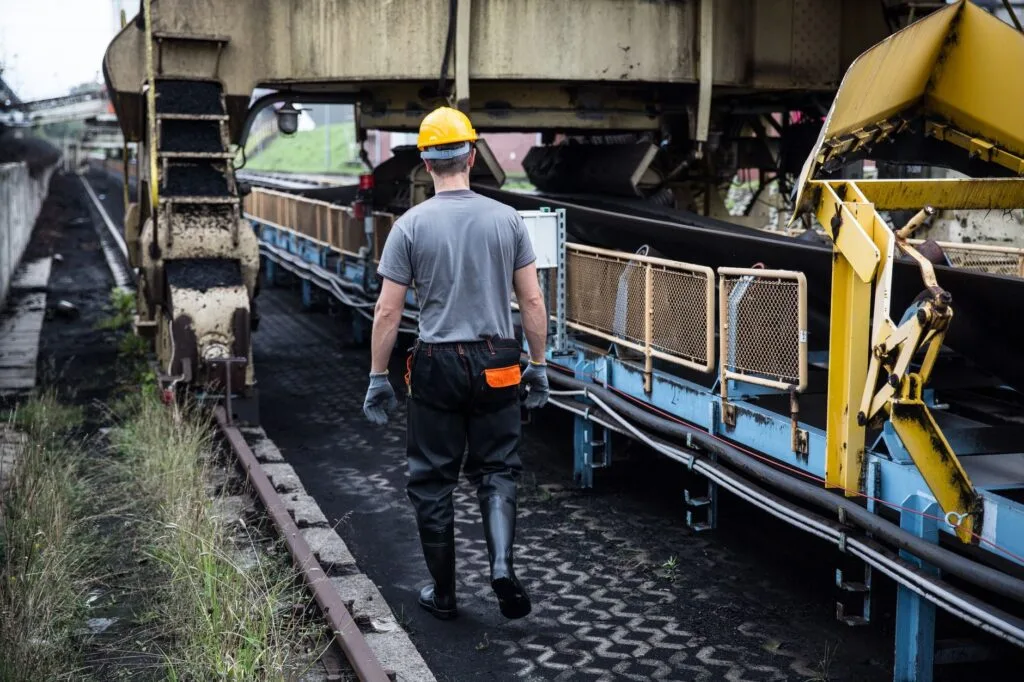 A worker in safety gear examines industrial machinery in an outdoor setting, showcasing industry work.
