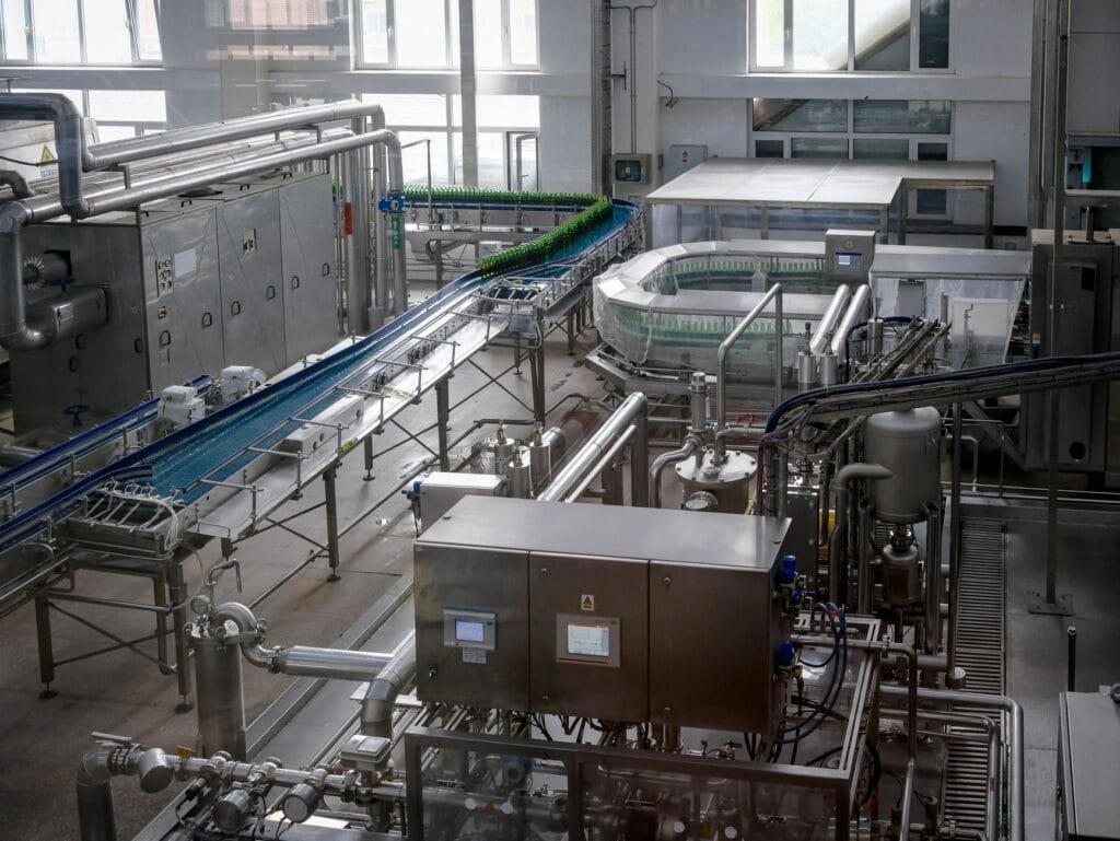 Interior view of an automated beverage bottling factory with machinery and conveyor belts.