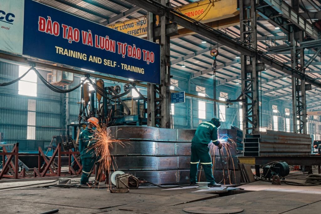 Workers weld metal structures in a bustling industrial factory, showcasing a dynamic work environment.