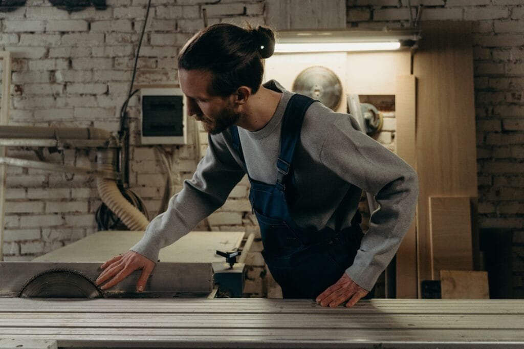 Man in denim overalls operating a circular saw in a woodwork shop.