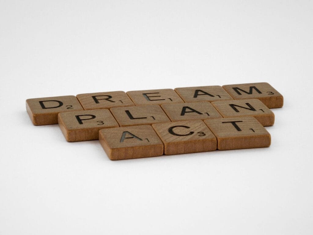 Wooden Scrabble tiles forming the motivational words: Dream, Plan, Act on white background.