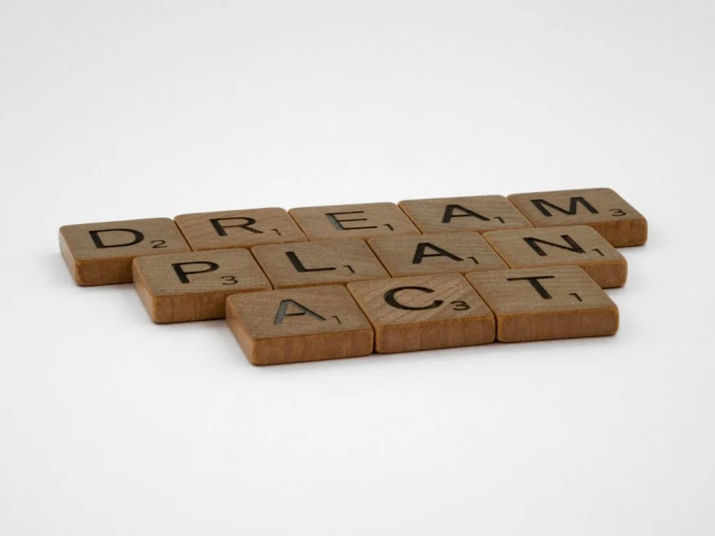 Wooden Scrabble tiles forming the motivational words: Dream, Plan, Act on white background.