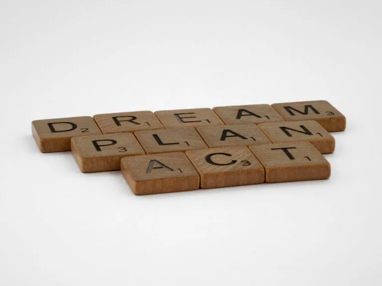 Wooden Scrabble tiles forming the motivational words: Dream, Plan, Act on white background.