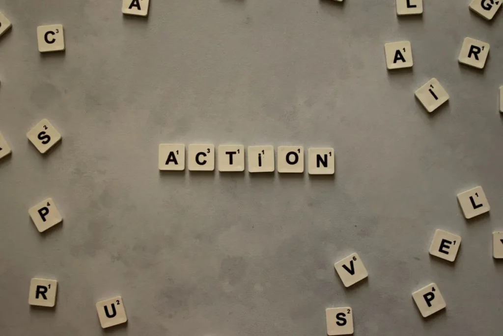 Flat lay of Scrabble tiles spelling 'Action' on a gray background, surrounded by random letters.